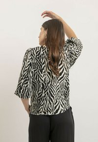 Haut en imprimé zèbre noir et blanc avec des manches bouffantes 3/4 et une coupe décontractée. Le tissu semble lisse avec un léger éclat.