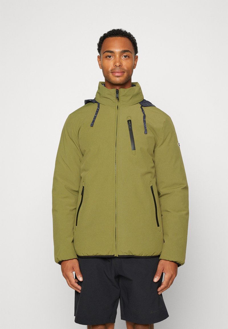 Chaqueta acolchada de color verde olivo con cuello alto, cierre frontal con cremallera y detalles en negro. Cuenta con dos bolsillos laterales y cremalleras expuestas.