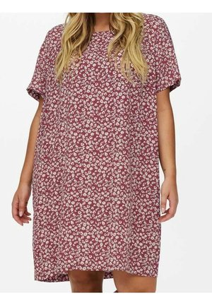 Mujer que lleva un vestido suelto de manga corta hasta la rodilla con un patrón floral rosa y blanco y cabello rubio ondulado.