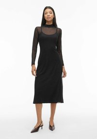 Melna midi kleita ar garām caurspīdīgām piedurknēm, apaļu kakla izgriezumu un regulējamām siksniņām. Gluda tekstūra un pieguloša siluets ar sānu šķēluma detaļu.