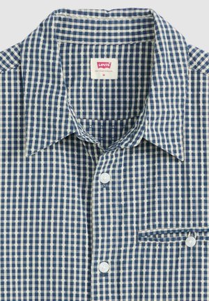 Camisa de cuadro azul y blanco, con botones y un cuello, que cuenta con un bolsillo en el pecho y una textura de tela suave. Los botones blancos acentúan la parte delantera.