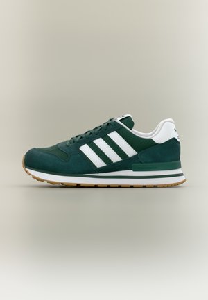 Ciemnozielony sneaker Adidas z białymi paskami, białą zakładką na pięcie, gumową podeszwą i sznurówkami, pokazany z profilu na neutralnym tle.