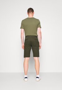 T-shirt vert olive et shorts assortis avec deux poches arrière. Texture de tissu lisse, shorts arrivant aux genoux, et baskets blanches avec des accents bleu marine.