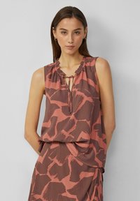 Blouse sans manches marron avec un motif abstrait rose, encolure froncée et ouverture en forme de clé. Tissu doux et coupe décontractée.