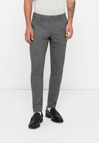 Pantalones grises a cuadros con un corte ajustado, elaborados en una tela suave, con cierre de botón y bolsillos frontales planos, combinados con mocasines negros.