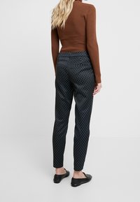 Haut à manches longues côtelé marron associé à un pantalon noir à motifs avec un design en losange. Tissu lisse, coupe près du corps, longueur aux chevilles.