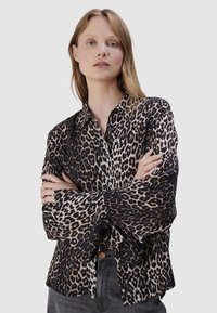 Tijgerprint shirt in zwart en beige, met een kraag, knoopsluiting en brede mouwen. De stof heeft een zachte textuur.