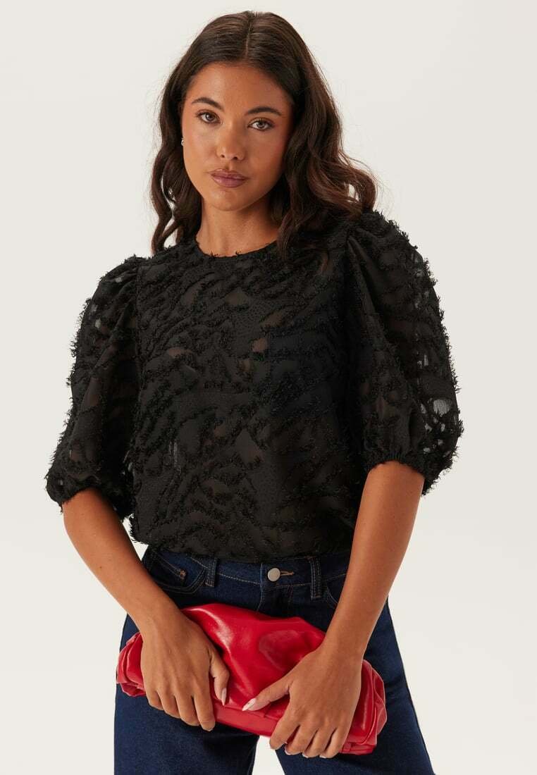 Blusa nera con texture, maniche a sbuffo e motivo floreale, abbinata a una pochette rossa e jeans di denim. tessuto liscio con dettagli di design a strati.