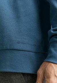 Felpa in cotone blu con una finitura testurizzata, caratterizzata da un logo discreto all'orlo e comodi polsini a costine.