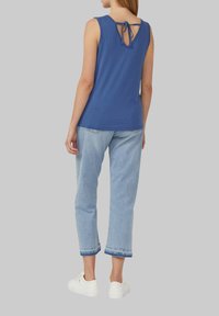 Blaues ärmelloses Oberteil mit einem Bindedetail auf der Rückseite, kombiniert mit hellblauen cropped Jeans mit fransigen Säumen und weißen Turnschuhen.