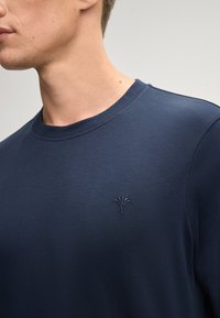 Dunkelblaues Rundhals-Sweatshirt aus weichem Material, mit einem dezenten gestickten Design auf der linken Brust. Rippkragen und -manschetten.