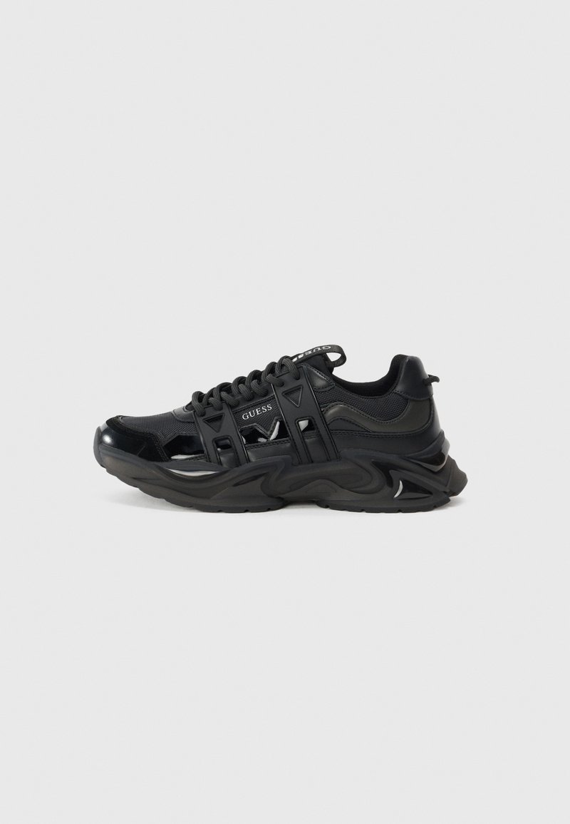 Black athletic sneakers featuring a glossy finish, mesh and synthetic material, chunky wavy sole, and cut-out accents. Logo on tongue.