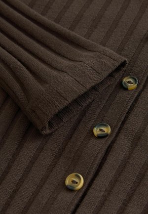 Tmavě hnědá, žebrovaná látka s přehnutým manžetou a třemi kulatými knoflíky v kontrastních barvách, ukazující texturu a designové detaily.