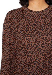 Haut en tricot marron avec un motif léopard noir, présentant un col rond et des détails de couture visibles aux épaules.