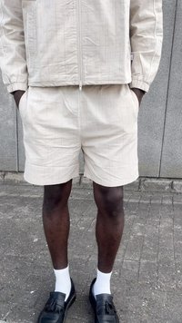 Beige topattu takki, johon kuuluu samat haalarit, joissa on teksturoitu design. Mustat loafersit, joissa on tupsut, ja valkoiset sukat.