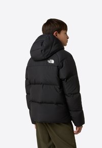 Fekete kapucnis pufi dzseki, steppelt mintázattal és logóval a hátoldalán. Simább, fényes felületű, laza fazonú.