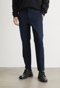 Navy blue trousers with a relaxed fit, elastic drawstring waistband, and side pockets, paired with black leather lace-up shoes.