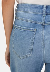 Jeans in denim azzurro chiaro con vita alta, dotati di una tasca posteriore e dettagli di cucitura visibili. Il tessuto sembra morbido e leggermente sbiadito.