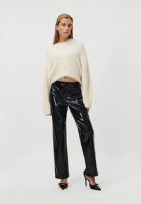 Pull en peluche blanc, court, avec des manches longues, associé à un pantalon en cuir verni noir taille haute et des escarpins noirs à bout pointu.