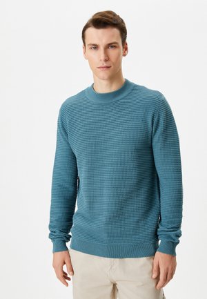 Suéter de punto en azul verdoso con cuello redondo acanalado y patrón texturizado. Mangas largas con puños acanalados y dobladillo, presentando un ajuste estructurado.