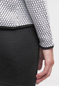 Czarna dopasowana spódnica zestawiona z teksturowaną, białą i czarną bluzką z długim rękawem, charakteryzującą się przylegającym krojem i kontrastowymi lamówkami.