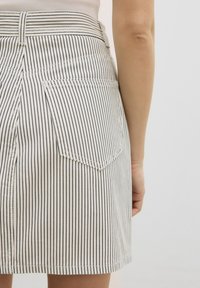 Gestreepte katoenen rok met verticale zwarte strepen op een witte achtergrond, voorzien van twee achterzakken en een zoom die halverwege de dij valt.