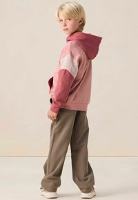 Haut à capuche en coloris rose en blocs, avec une capuche, présentant une manche plus claire et des teintes plus foncées, associé à un pantalon gris ample.