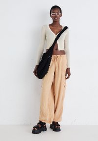 Light beige ribbed cropped cardigan, loose peach wide-leg trousers, black textured shoulder bag, and chunky black sandals.