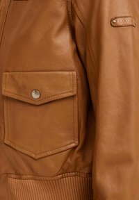 Giacca in pelle marrone con tasca frontale a soffietto fissata da un bottone a pressione in metallo e vita elastica ribbed.