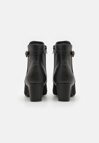 Botines de cuero negro con tacón cuadrado, que cuentan con una cremallera lateral y una correa decorativa con una hebilla dorada. Textura suave.