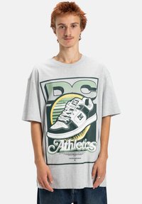 Szary, oversize t-shirt z graficznym nadrukiem sneakersa, wyraźnym logo "DC" oraz tekstem "Athletics" w kolorze zielonym i czarnym. Krótkie rękawy.