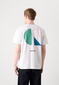 Balta medvilninė marškinė su dideliu geometriniu raštu ant nugaros, kurioje dominuoja žalia, mėlyna ir rožinė spalvos, o apačioje išspausdintas užrašas "calvin klein".