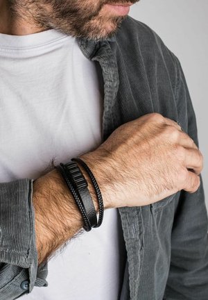 Black leather and braided material bracelets on a wrist, showcasing a textured design with a rectangular accent piece.