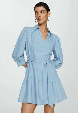 Robe en denim bleu clair avec un décolleté en V, des manches bouffantes et une taille ceinturée. Elle présente une jupe évasée et une texture lisse.