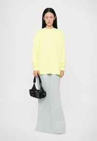 Neon yellow long-sleeve shirt, loose fit, paired with a pale blue denim maxi skirt. Black handbag with silver hardware accents in hand.
