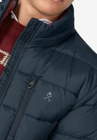 Chaqueta de abrigo en color navy con cierre de cremallera, que presenta un logo en el pecho, diseño acolchado y un cuello alto, hecha de material resistente al agua.