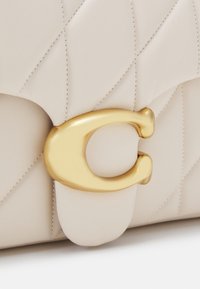 Beżowa pikowana skórzana torba z dużym złotym metalowym zapięciem w kształcie litery "C" na przedniej klapie.