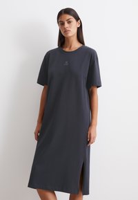 Czarna bawełniana sukienka T-shirt z krótkimi rękawami, o prostym kroju i bocznym rozcięciem. Dyskretne haftowanie "M OP" na klatce piersiowej.