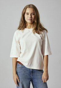 T-shirt rosa chiaro a maniche corte realizzato in morbido tessuto di cotone, con scollatura rotonda e vestibilità comoda, abbinato a jeans blu.