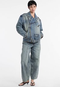 Completo giacca e pantaloni in denim blu sbiadito, con gambe larghe, vita con cintura e numerose tasche. Tessuto liscio con vestibilità rilassata.