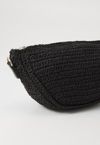 Borsa nera all'uncinetto con forma arrotondata, superficie texture e un accento in hardware dorato. Presenta un attacco per una tracolla laterale.
