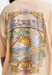 Γραφικό T-shirt σε απαλό ροδάκινο με πολύχρωμο σχέδιο εμπνευσμένο από τη φύση, που περιλαμβάνει φοίνικες, ήλιο, καταρράκτη και λουλούδια. Κείμενο "Billabong" με έντονα στοιχεία.