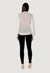 Cardigan leggero in crema con maniche texturizzate e schiena trasparente, abbinato a leggings neri e tacchi nude. Design semplice e moderno.