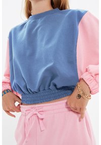 Felpa color-block con un corpo blu e maniche rosa. Presenta una vita arricciata, colletto a costine e una texture in cotone morbido.