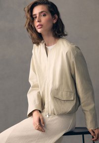 Licht beige bomberjack met een ritssluiting aan de voorkant, twee opgestikte zakken en een comfortabele pasvorm, gecombineerd met een bijpassende gemêleerde rok.