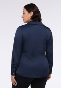 Námořnickomodrá košile s dlouhým rukávem a límečkem, hladký povrch, knoflíkové detaily na rukávech, přiléhavý střih a zakřivený lem.