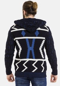 Gestickter pullover mit blau-weißem Muster, der eine strukturierte Gestaltung aufweist, mit Zickzack-Elementen sowie gerippten Bündchen und Saum.