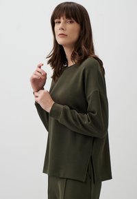 Felpa a maniche lunghe verde scuro con una vestibilità ampia, fessure laterali e texture morbida, impreziosita da maniche a taglio dritto e scollo rotondo.