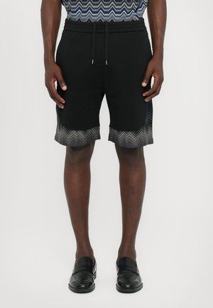  Sorte shorts med snor i taljen, prydet med et zigzag mønster i grå ved kanten. Fremstillet af blødt stof, knælang model.