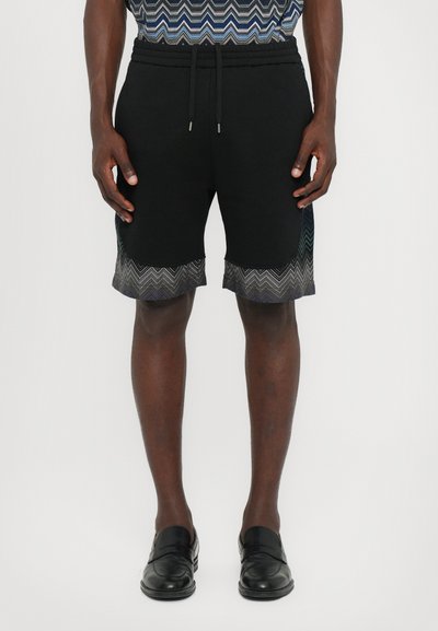  Sorte shorts med snor i taljen, prydet med et zigzag mønster i grå ved kanten. Fremstillet af blødt stof, knælang model.